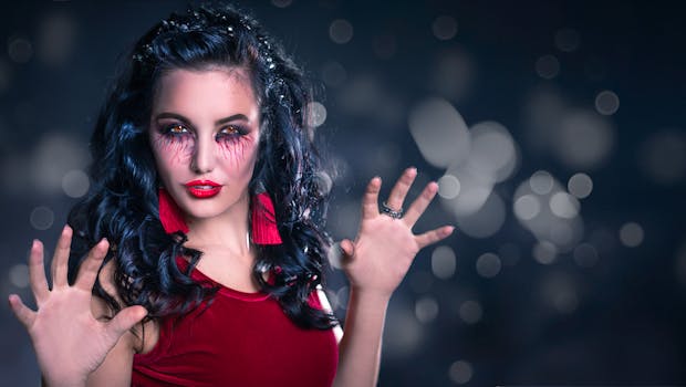 Femme avec des cheveux noirs ondulés, maquillage dramatique et robe rouge, posant avec une expression confiante.